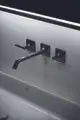 Wandmontierte Waschtischarmatur in der Farbe Magnetic Grey von Ideal Standard, mit zwei Hebelgriffen und einem langen, gebogenen Auslauf vor glatter Wand.